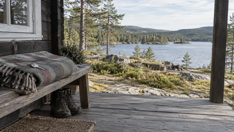 Hyttenøkkel på et ullpledd og turstøvler på en veranda ved vannet.